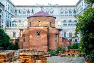 St. George Rotunda, an ancient red brick church surrounded by modern buildings in Sofia, Bulgaria, under a clear sky.